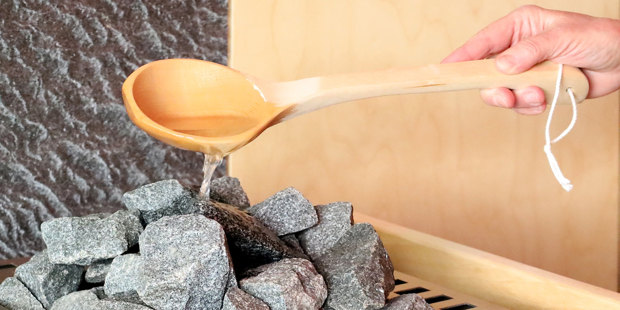 Saunaaufguss mit Holzkelle über Saunasteine